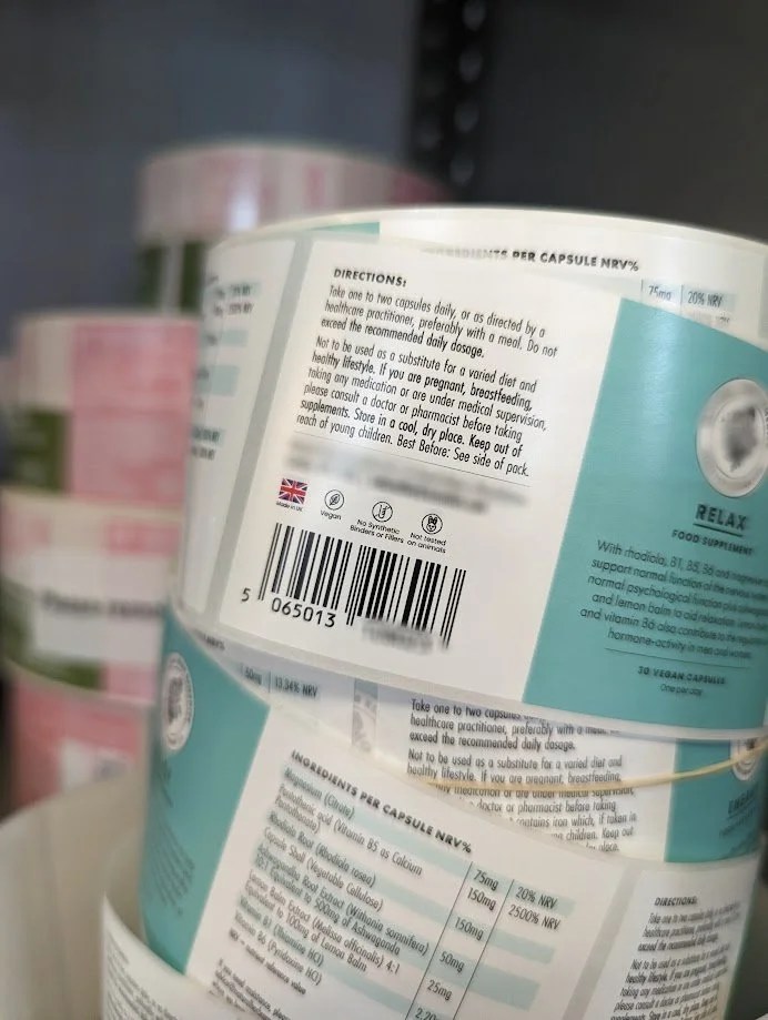 A container of dietary supplements with directions and ingredients printed on the label, placed on a shelf with other supplement containers in the background.